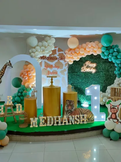 A modern safari theme using gold pedestals and a clean, arched backdrop against a grass wall. A neon sign and marquee letters add a bright, celebratory touch.
