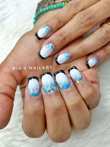 A Russian-style inbuilt French manicure. This technique creates a sharp, deep smile line, seen here with a black tip and blue glitter accents.