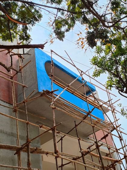 'Project 83' standing tall during construction, wrapped in traditional bamboo scaffolding. This photo captures the building taking shape, showcasing the bold blue balcony feature against the raw concrete and brick structure.