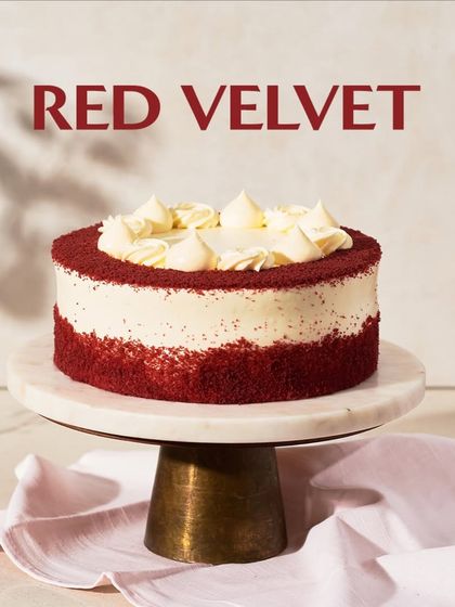 My classic Red Velvet cake, presented on a marble and wood stand. I frost it with a generous amount of rich cream cheese frosting and a border of soft red velvet crumbs.