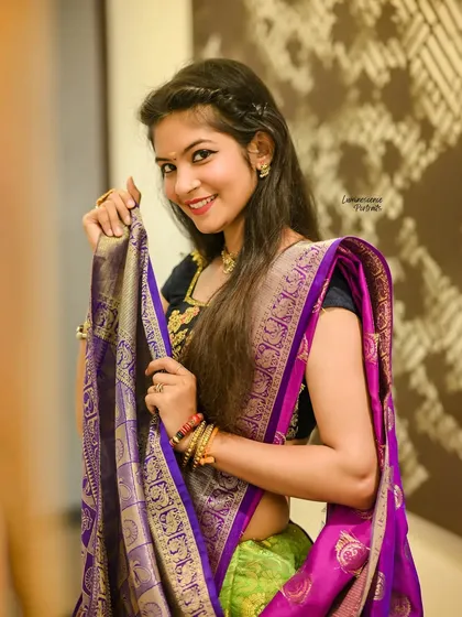 A playful and happy portrait, with the model holding the pallu of her purple and green half-saree.