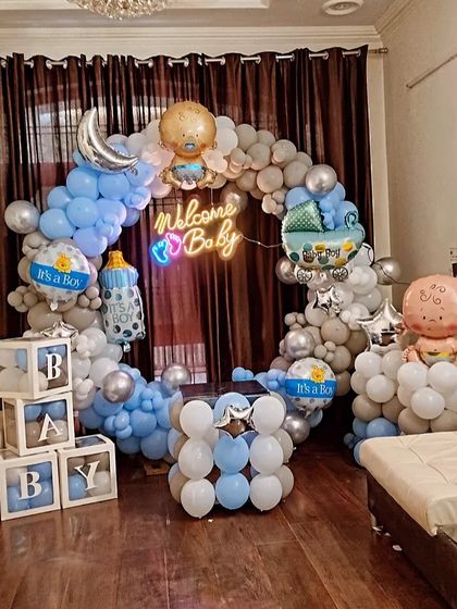 A full room decoration for a 'Welcome Baby' party. The setup includes a circular balloon arch, 'BABY' blocks, and various themed foil balloons like a baby bottle and a moon.
