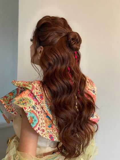 A textured top knot with soft waves, perfect for a Mehendi look. The pink braided threads add a pop of color that ties the whole look together.