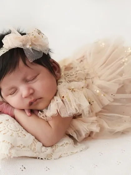 Simply angelic. This close-up shot highlights the delicate features of a newborn, with a soft, lacy outfit and a simple background. It's a timeless portrait that focuses purely on the baby.