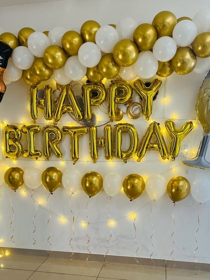 A classic adult birthday theme with a gold and white balloon arch. The decoration is accented with whiskey bottle and glass foil balloons and warm fairy lights.