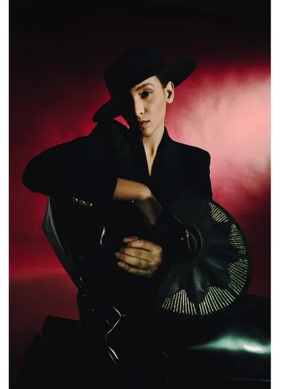 A portrait from the 'Levels of Power' series, featuring a model in a black hat and suit against a smoky red background. The dramatic lighting and commanding pose evoke a sense of authority and mystery.