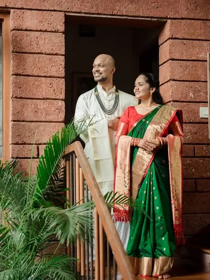 A beautifully composed shot of the couple standing on a staircase, framed by the architecture of their home. Their traditional attire stands out against the rustic brick.