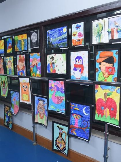 Another angle of our gallery wall, filled with colorful paintings by students of all ages. You can see a variety of mediums and themes, from nature scenes to imaginative character drawings.