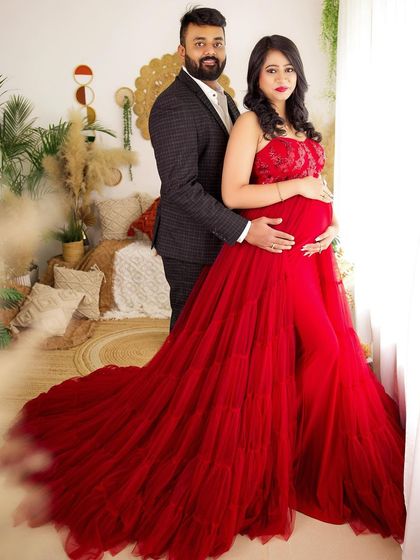 A full-length portrait of the couple against the warm, natural textures of the boho set. The red gown provides a stunning pop of color.
