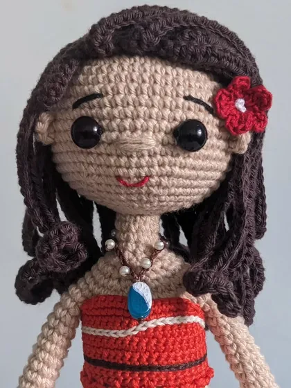 A close-up of the Moana doll's face, showing her wavy hair and the red flower.
