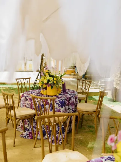 The guest seating area under a flowing white canopy. The tables are dressed in purple floral-print linens with bright yellow centerpieces, creating a beautiful contrast for this outdoor Haldi.