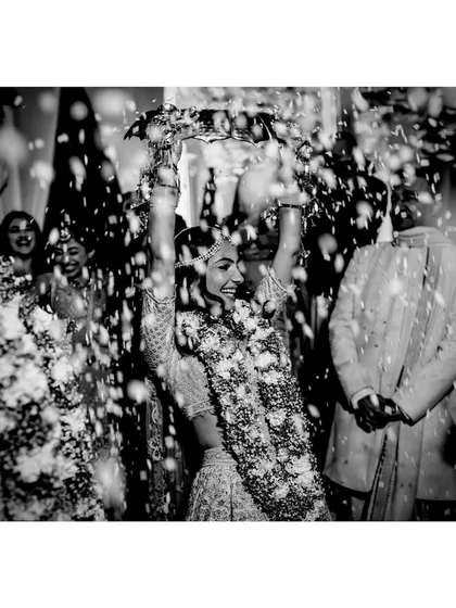 A bride celebrates after her wedding ceremony, showered in petals. This dynamic black and white photo captures the pure, unadulterated joy of the moment.