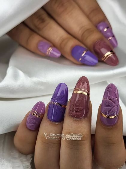 Classy Christmas fall nails. This set uses a beautiful palette of purples and features embossed leaves and gold chrome accents for a cozy and luxurious feel.