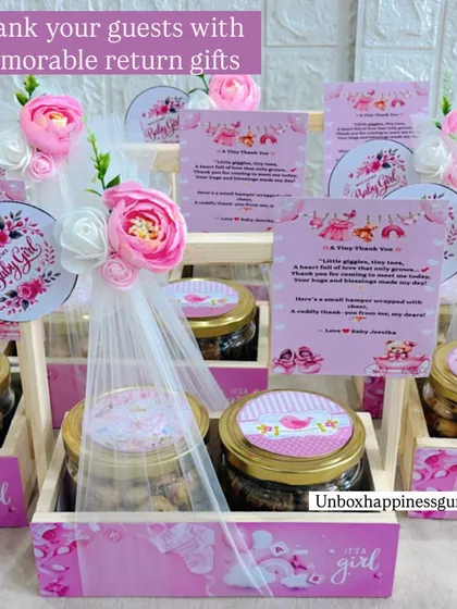 These memorable return gifts are perfect for a baby girl's announcement, featuring personalized cards and jars of treats in a decorated wooden crate.