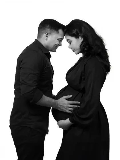 An intimate black and white portrait of a couple. The foreheads touching and hands on the bump create a circle of love, a classic pose that is full of emotion.