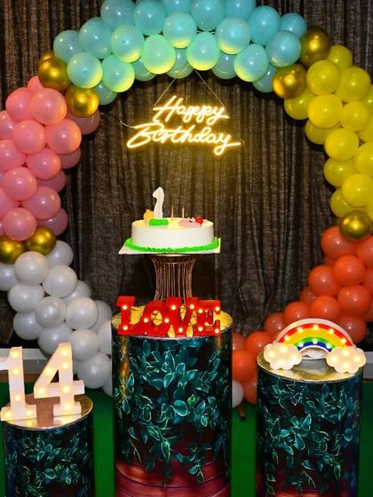 A colorful birthday setup for a 14th birthday. The circular balloon arch uses a rainbow of colors, complemented by a neon sign and themed pedestals.