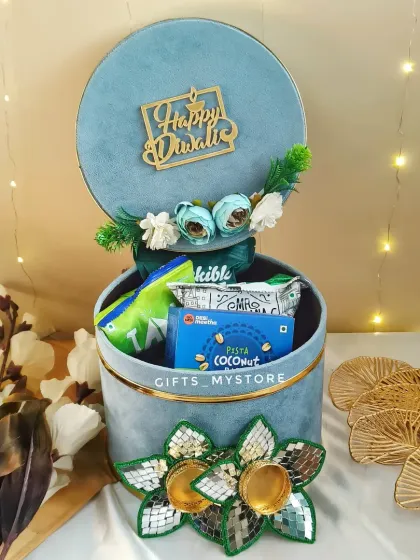 A side view of the elegant light blue velvet hamper box, showing the pretty floral decorations and the 'Happy Diwali' tag.