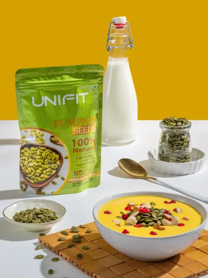 A packet of Unifit pumpkin seeds, styled with a bowl of pumpkin soup and a bottle of milk to show a use case.
