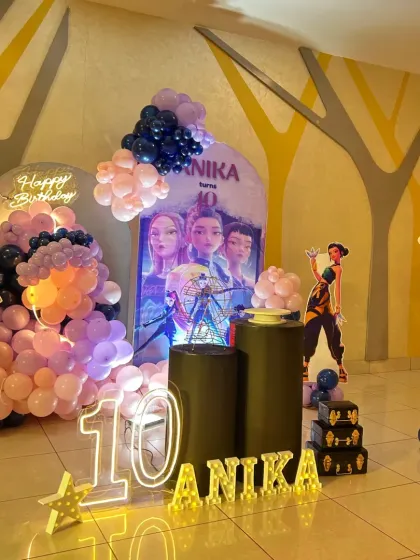 A wide view of a large-scale 'Huntrix' themed party for Anika's 10th birthday, with multiple backdrops and life-sized character cutouts.