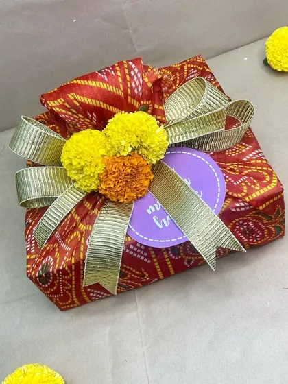 Holi Hai. A simple yet vibrant gift wrapped in traditional bandhani paper and topped with marigolds, perfect for spreading festive cheer.
