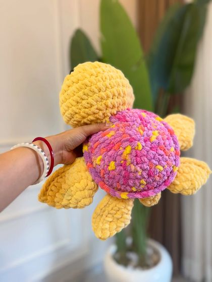 A side view of our yellow and pink amigurumi sea turtle, showing its little flippers and soft, patterned shell.