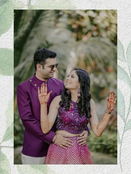 A candid moment from a mehendi function. The bride shows off her henna-adorned hands while sharing a happy glance with her groom, capturing the fun and tradition of the day.