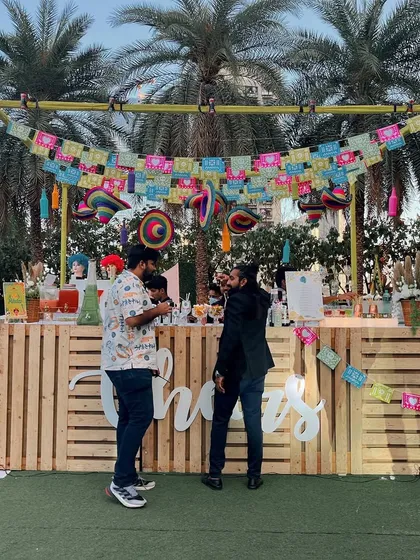 A rustic and colorful sundowner bar. The wooden pallet bar, festive banners, and outdoor setting create a relaxed and cheerful atmosphere.
