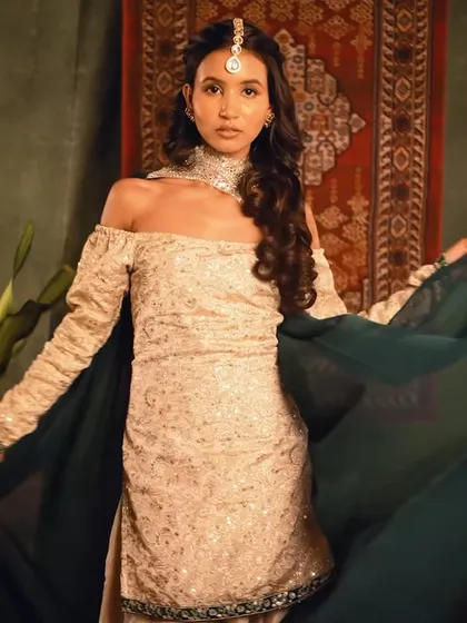 A full-length view of the Heeramandi-inspired look. The off-shoulder outfit is paired with a romantic, side-swept hairstyle, creating a look of historical elegance.