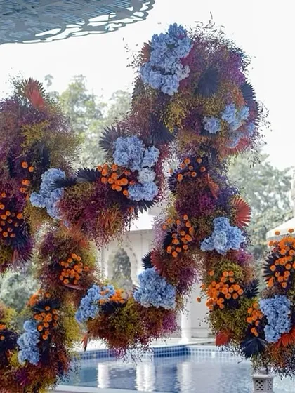 An abstract, free-floating floral sculpture named 'Azure Ochre'. The design mimics the texture and movement of volcanic lava, using a vibrant and unconventional color palette of blue, orange, and deep reds.