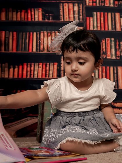 For the little book lover. This girl is exploring a picture book in a cozy library setting, a perfect theme for capturing a child's curious and quiet side.