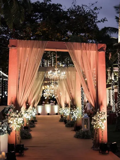 An elegant and sophisticated entrance with soft peach drapes, chandeliers, and white floral arrangements.