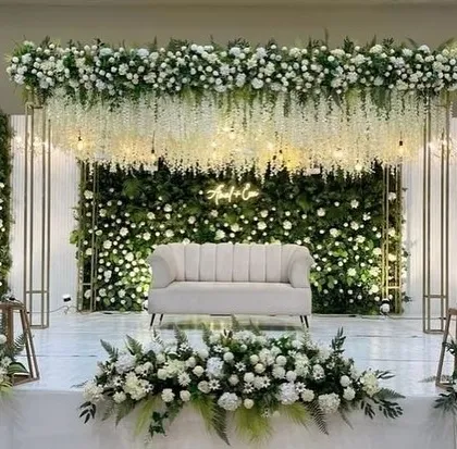 For a sophisticated engagement or reception, nothing beats a classic white and green theme. This stage features a lush green wall covered in white roses, with hanging wisteria flowers and a custom neon sign, creating an elegant and romantic setting.