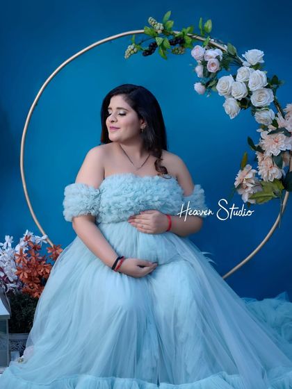 A serene portrait against a rich blue backdrop. The mother-to-be cradles her bump in a beautiful off-shoulder tulle gown, creating a peaceful and elegant image.