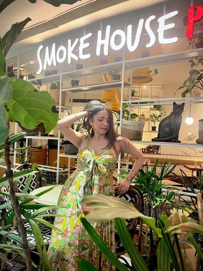 A dress that feels as light as a flower. Posing in a floral maxi dress at Smoke House Deli, surrounded by lush greenery.