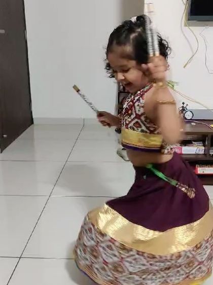 A candid shot of a little girl playing Dandiya in her custom-made Garba outfit, full of joy and energy.