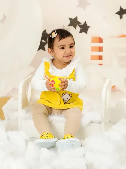 A happy baby girl in a yellow dress, surrounded by star and cloud props, enjoying her first birthday photoshoot.