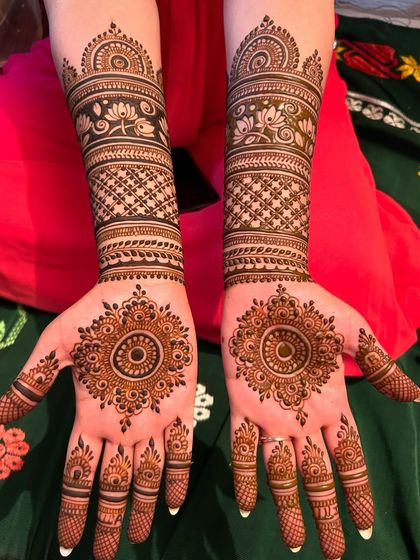 This is a classic festive design featuring a detailed mandala on the palm. The arms are adorned with bands of lotus flowers and fine-line check patterns, extending up to the mid-forearm.
