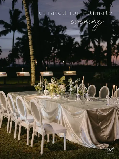 An elegant dinner table set for a seaside celebration, with the dusky sky and palm trees creating a beautiful natural backdrop.