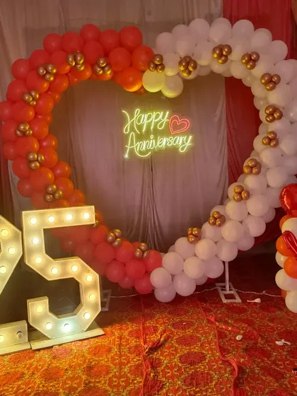 25th anniversary jaise bade function ke liye hum grand decoration karte hain. Ismein red aur white balloons ka heart shape arch, '25' number ke light letters, aur 'Happy Anniversary' ka neon sign shaamil hai.
