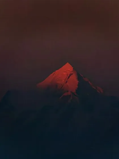 The last light of sunset hits a single mountain peak in Ranikhet, making it glow red against the darkening range. This is a dramatic and fleeting moment captured in the Himalayas.