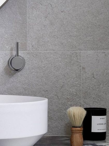 Design is in the details. This close-up shows a minimalist bathroom with a textured gray tile wall, a sleek chrome faucet, and a modern vessel sink. The clean lines and simple material palette reflect our belief in refined, intricate detailing.