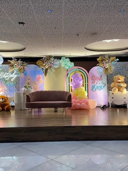 A full view of a spectacular pastel rainbow stage I designed for a large baby shower. The setup features a "Girl or Boy?" reveal sign, a crescent moon prop, multiple backdrops, and a decorative candy cart, all tied together with a vibrant color scheme.