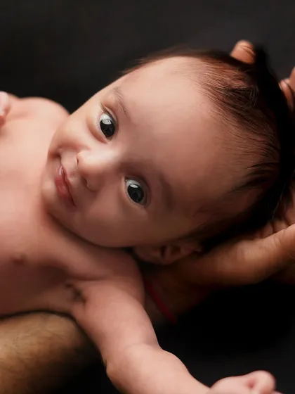 A newborn looks up with wide, curious eyes while being held safely in their parent's hands. This shot captures a moment of early connection and awareness.