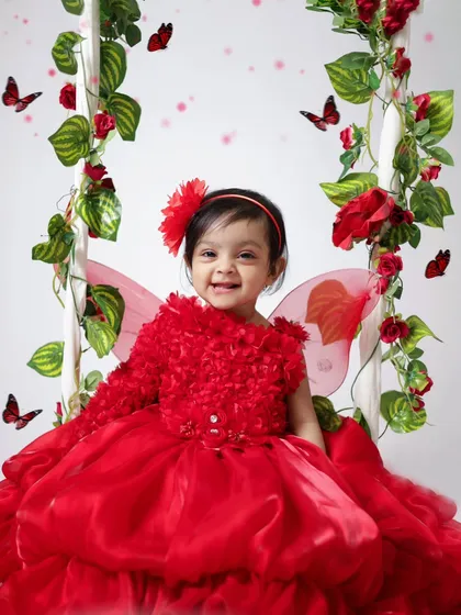 Dressed as a little red fairy with butterfly wings, this baby girl's smile is magical. We use props like this floral swing to create enchanting fairy-tale themes for first birthdays.