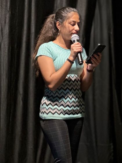 A participant reads her piece from a phone, sharing her poetry or story with the audience. Our open mic is a welcoming space for first time performers and seasoned artists alike.