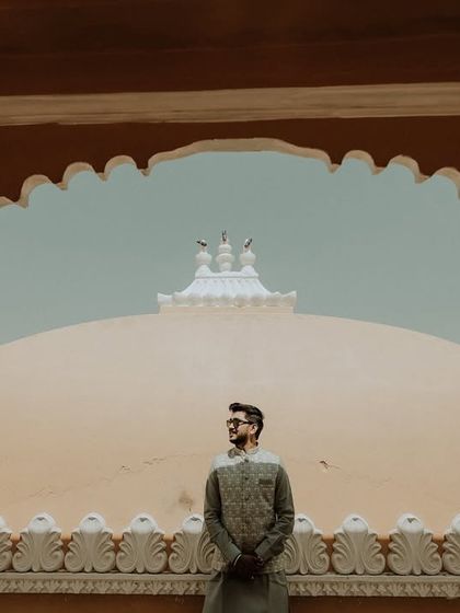 The groom stands framed by a traditional archway, creating a strong and stylish solo portrait. The composition highlights both the individual and the grandeur of the location.