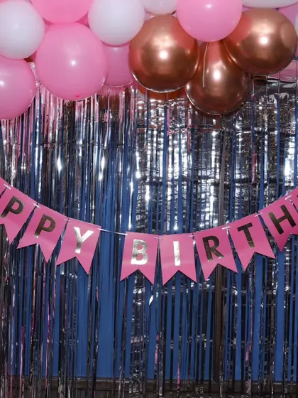 A close-up of the pink 'Happy Birthday' banner against a silver fringe curtain.