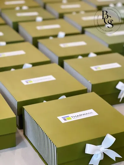 An example of branded corporate gifting. These olive green and white striped boxes feature the client's logo, "Tharwani Realty," prominently on the lid, and are finished with a clean white bow for a professional look.