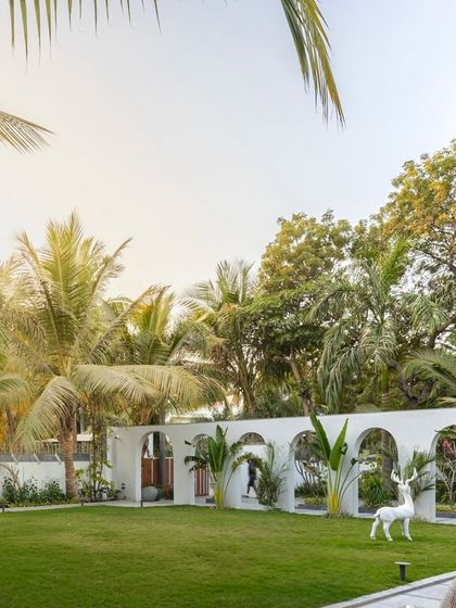 The arched wall at 'Tropical Manor' acts as a beautiful backdrop to the expansive lawn. The white deer sculpture adds a whimsical touch, while the surrounding coconut palms reinforce the tropical, regal atmosphere of the property.