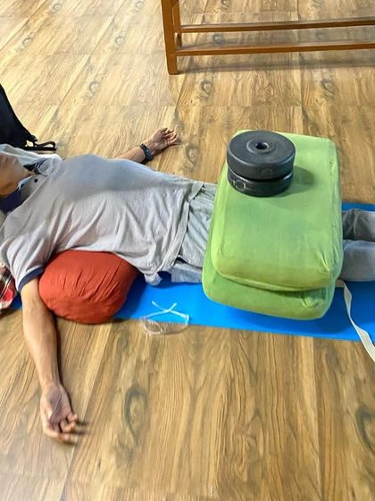 A restorative pose with weights on the thighs and a bolster under the head. The gentle weight helps to release the hip flexors and ground the body in Savasana (Corpse Pose).